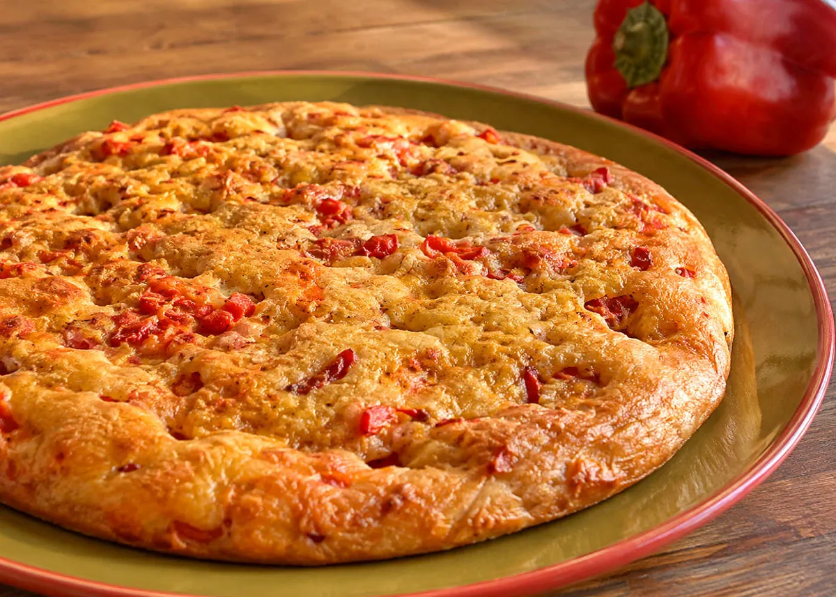 Schiacciata dorada de pimientos en un plato grande, salpicada de trozos de pimiento rojo