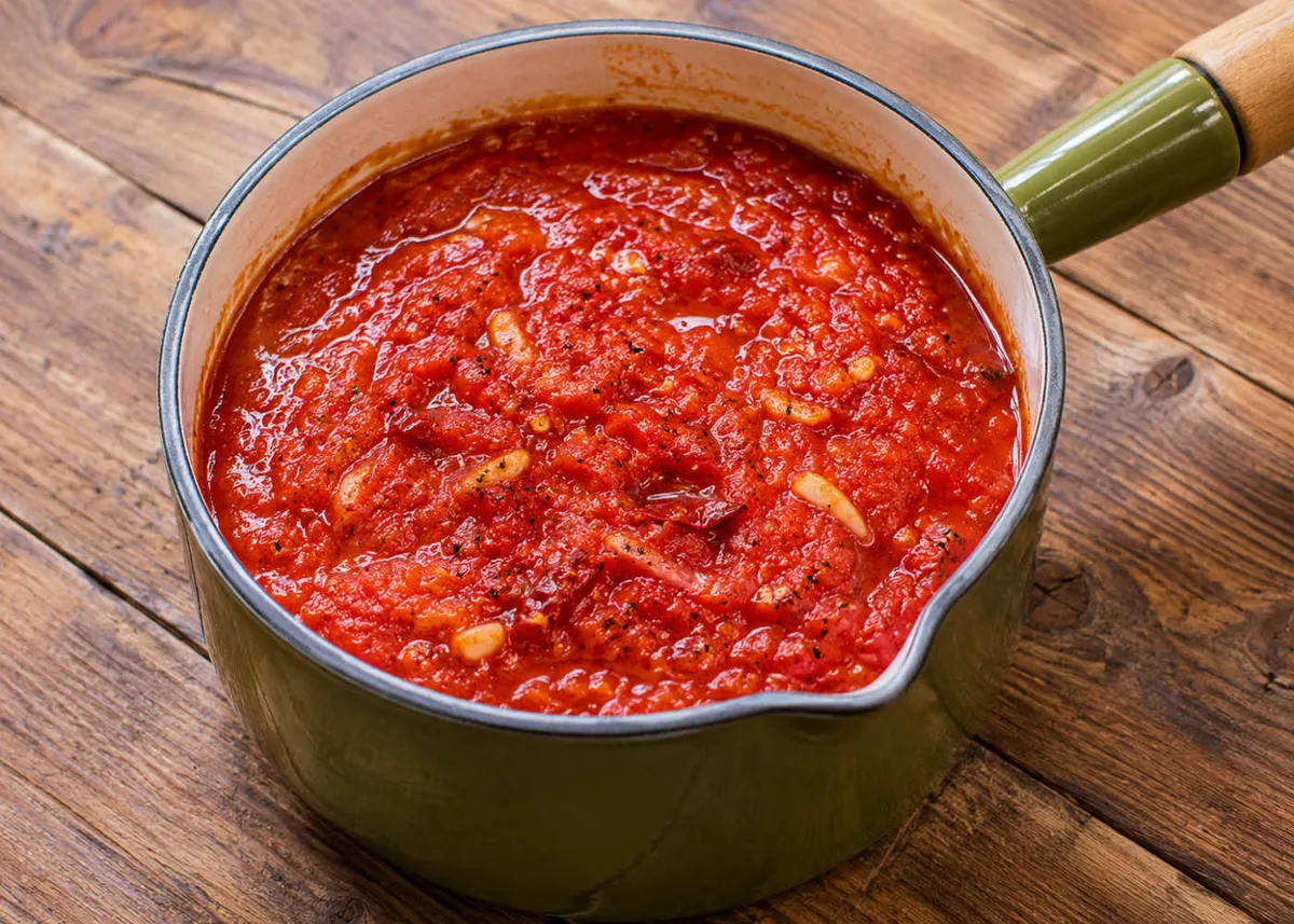 Cacerola de salsa de tomate arrabbiata picante de un rojo intenso sobre una mesa de madera